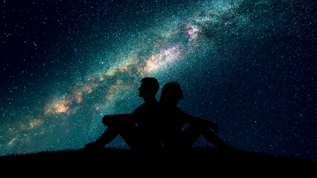 这对夫妇坐在草地上，背景是繁星点点的天空。时间流逝视频素材