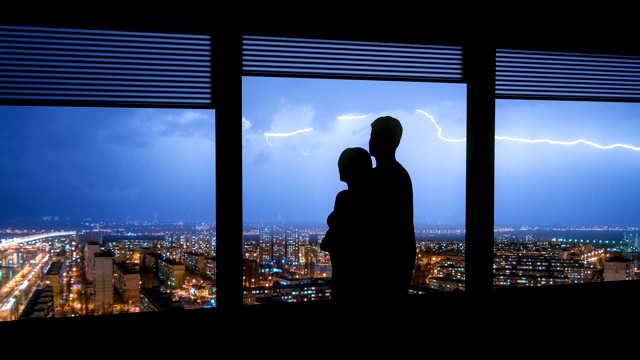 这对情侣站在窗前，面对城市上空的闪电。时间流逝视频素材