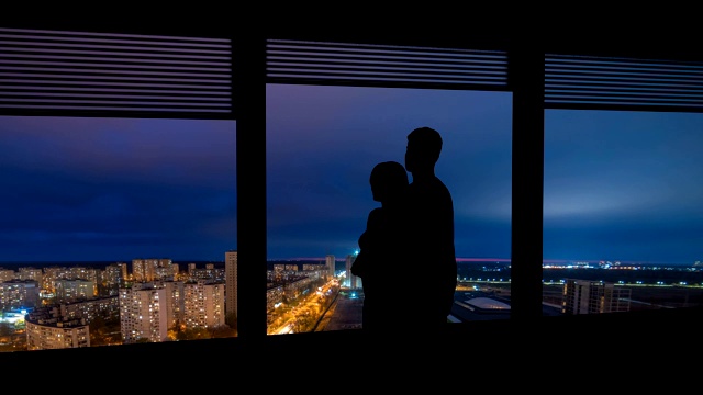 这个男人和女人站在有城市景观的窗户旁边。时间流逝视频素材