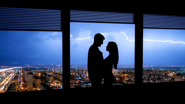 这对情侣站在以城市闪电为背景的窗户旁。时间流逝视频素材