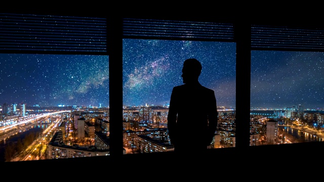 站在窗前的男人，背景是夜晚的城市。时间流逝视频素材