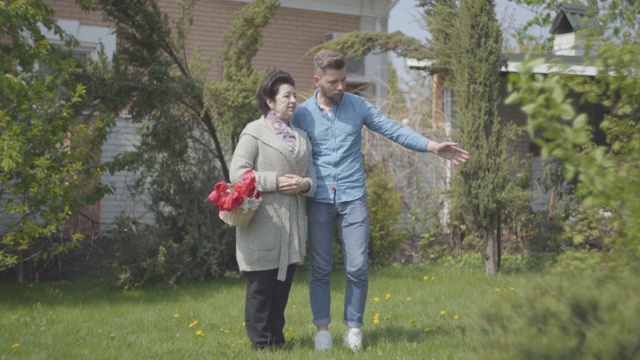 描绘一个成熟的女人拿着篮子和她的孙子在后院聊天。视频素材
