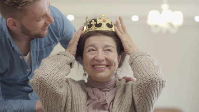 成年的孙子把王冠戴在奶奶的头上。视频素材