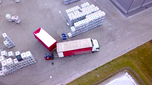 叉车在仓库外的大货架之间移动，并装载托盘。无人机拍摄的视频素材