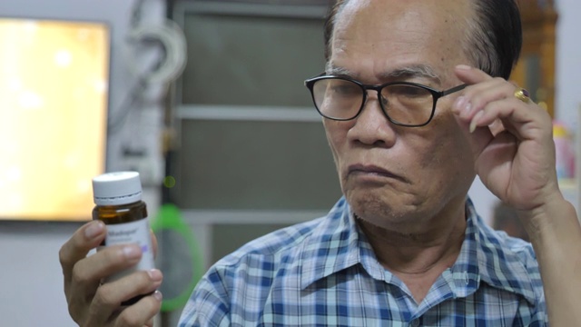 年长的亚洲男人戴上眼镜读她的处方瓶的场景视频素材