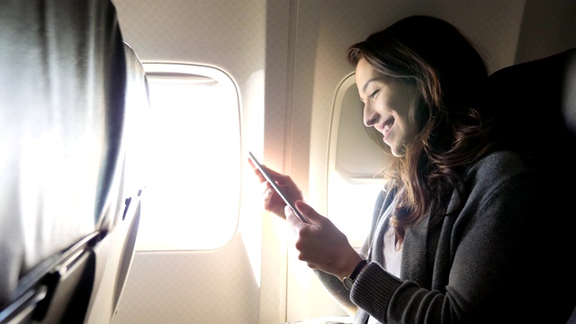 快乐的年轻白人女性在飞机上使用智能手机视频素材