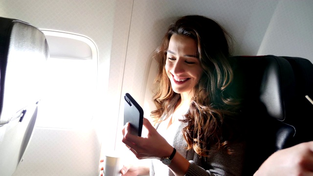 自信的年轻女子在飞机上使用智能手机视频素材