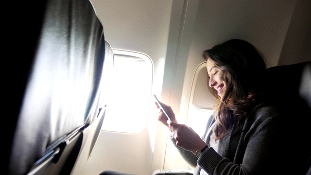 一名年轻女子在飞行中使用智能手机时大笑视频素材