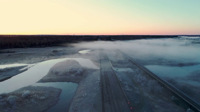 在一个寒冷的春天清晨，一辆轿车从浓雾中出现在明尼苏达州奇佩瓦国家森林的一条废弃的高速公路上。无人机视频与向后相机运动。视频下载