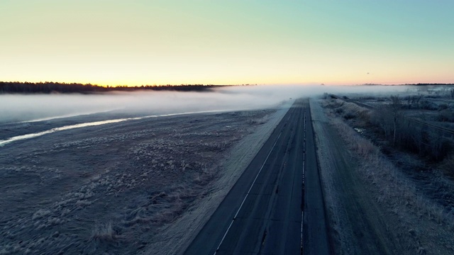 在明尼苏达州奇佩瓦国家森林，一辆汽车行驶在被雾覆盖的道路上，这是一个寒冷的春天清晨，雾霾弥漫。无人机视频配合前方摄像头运动，跟踪车辆行驶在路上。视频下载