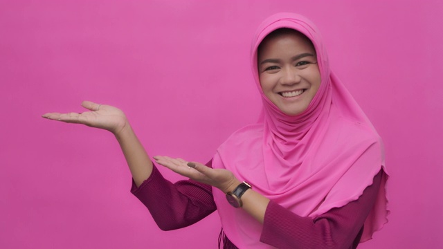SLO MO穆斯林妇女的肖像与手势指向你的标志粉红色的背景拷贝空间视频下载