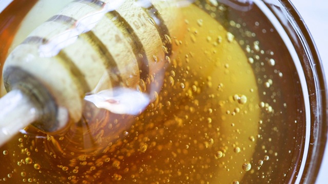 蜂蜜从玻璃罐里的蜂蜜勺中滴落。视频素材