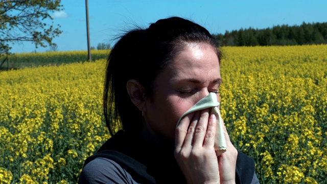 在油菜花地里打喷嚏的女人。花粉过敏的概念视频下载