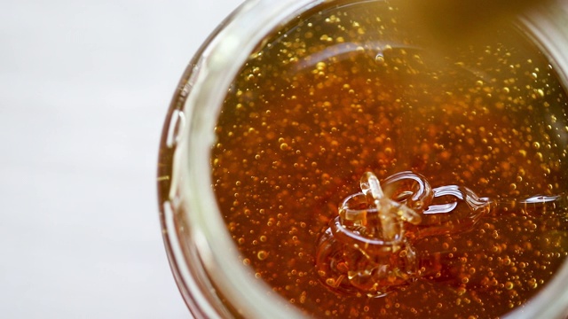 蜂蜜从玻璃罐里的蜂蜜勺中滴落。视频素材