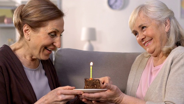 老妇人送生日蛋糕给朋友，女士许愿和吹蜡烛视频素材