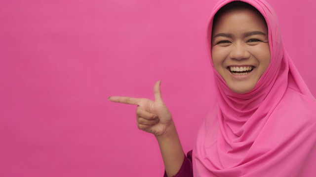 SLO MO穆斯林妇女的肖像与手势指向你的标志粉红色的背景拷贝空间视频素材