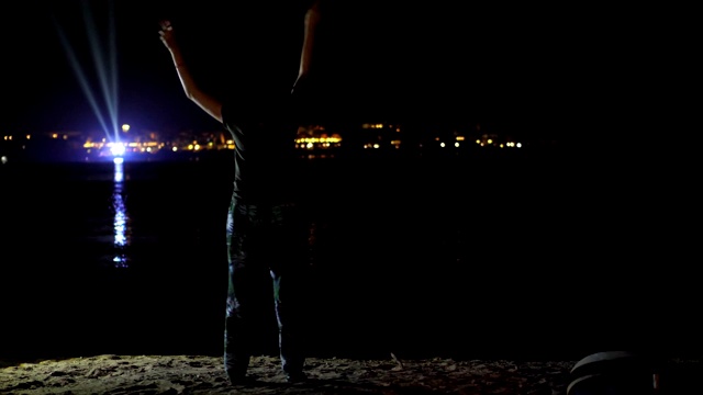 夜，一个女人在跳舞，从后面看。在水面上闪烁的城市灯光的映衬下视频素材