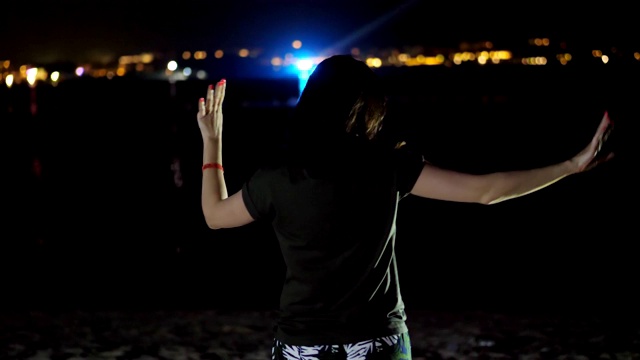 夜晚，一个女人在跳舞，从后面看。映衬着水面上城市的灯光视频素材