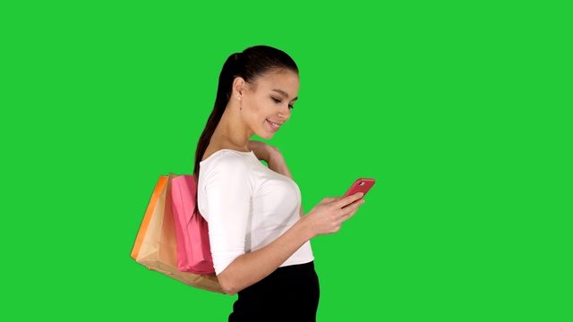漂亮的年轻女人用手机走路和拿着购物袋的绿色屏幕，色度键视频素材