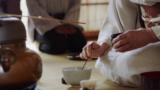 茶道主持人将茶叶从茶叶罐中舀入碗中，客人在一旁观看视频素材