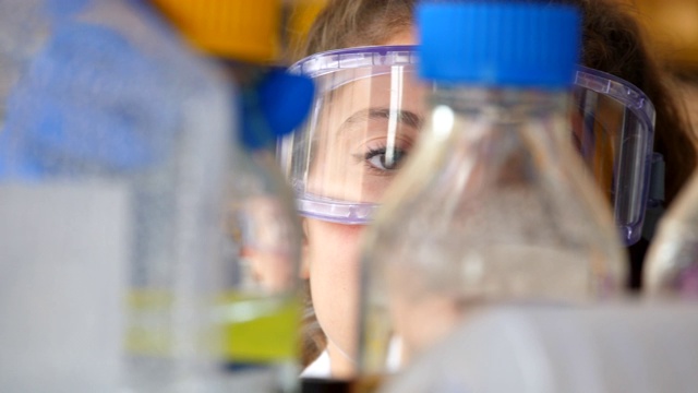 CU从实验室中戴着护目镜的女科学家的溶液瓶中查看视频下载