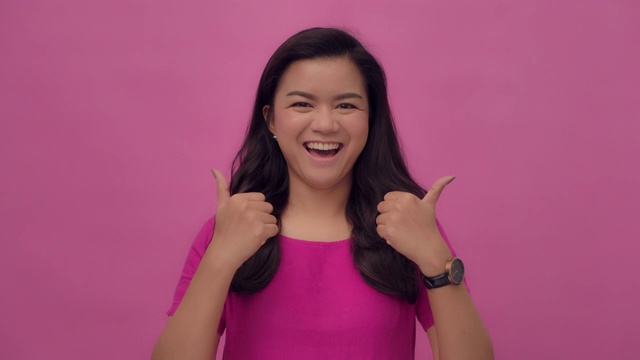 SLO MO肖像的年轻亚洲与一个幸福的微笑拇指向上的手势在粉红色的背景视频素材