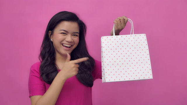 一个快乐的亚洲女人指着她手里拿着的购物袋视频素材