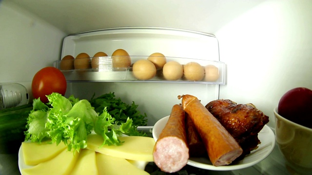 冰箱里的食物。在冰箱里找食物的女人。在肉和蔬菜之间选择。视频下载