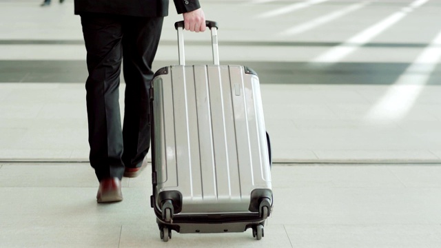跟随中景拍摄的一个不认识的商人走在机场大厅，拉着行李车行李箱视频素材