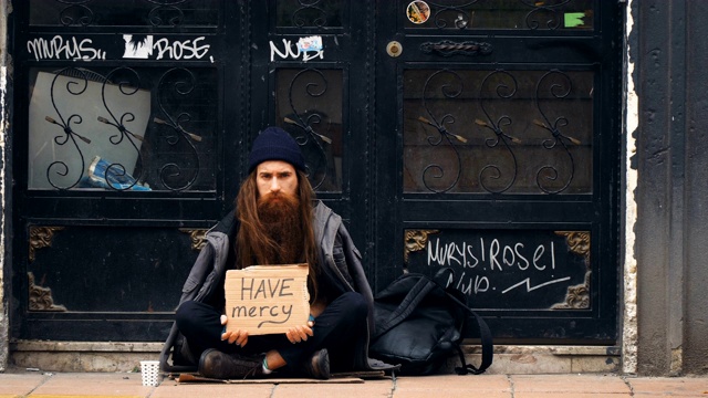 一个无家可归的人在拥挤的街道上拿着“救命”纸板乞讨视频下载