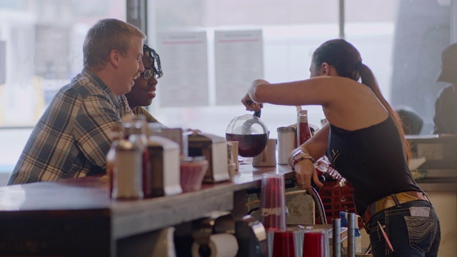 在一个正宗的餐厅柜台，服务员为年轻夫妇倒咖啡到咖啡杯里视频下载