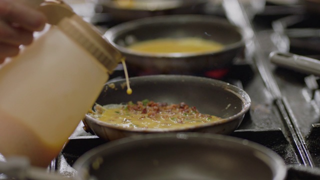 SLO MO:在一家商业餐厅的厨房里，专业厨师在燃烧的火炉上用平底锅炒鸡蛋和培根。视频素材