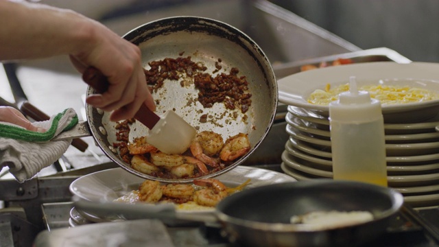 铜。在一个商业厨房里，专业的厨师将虾和脆培根片刮到一盘奶酪粗粉上视频素材