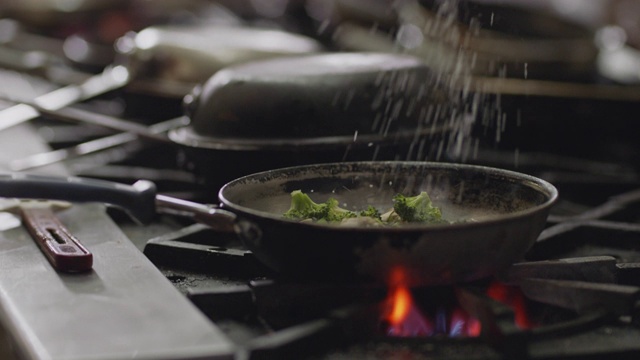 在一家商业餐厅的厨房里，专业厨师将香料洒在一个平底锅里的西兰花上。视频素材
