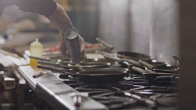 SLO MO专业厨师在一个商业厨房里的一个燃烧的炉子上的平底锅上喷洒烹饪喷雾。视频素材