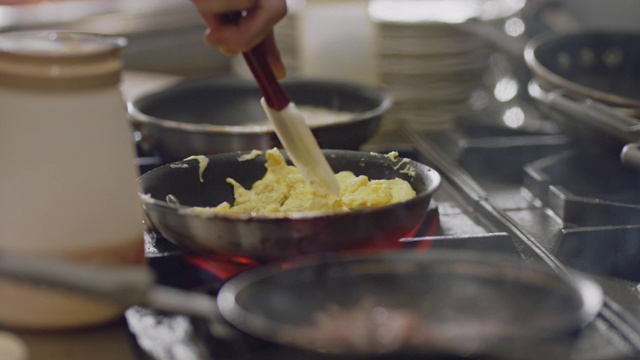 SLO MO:在一家商业餐厅的厨房里，专业厨师在燃烧的火炉上用平底锅炒鸡蛋。视频素材