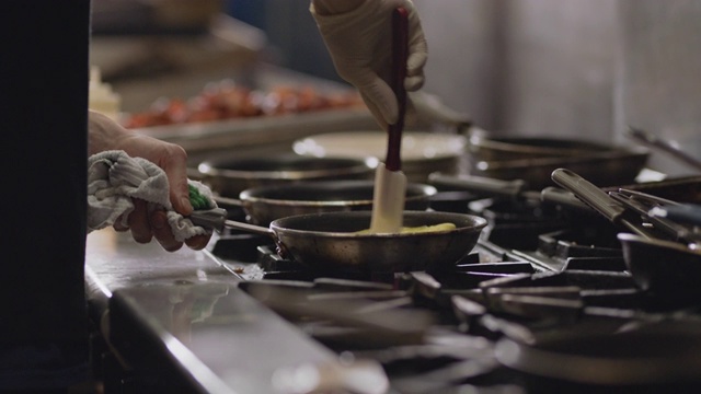 在一家餐馆的商业厨房里，专业厨师在一个燃烧的炉子上用平底锅烹饪煎蛋卷。视频素材