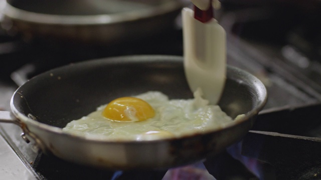在一间商业厨房里，专业厨师在一个燃烧的炉子上用平底锅煎鸡蛋。视频素材