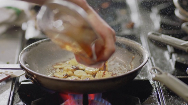 职业厨师在一家商业餐厅的厨房里，在燃烧的火炉上用平底锅煎香蕉。视频素材