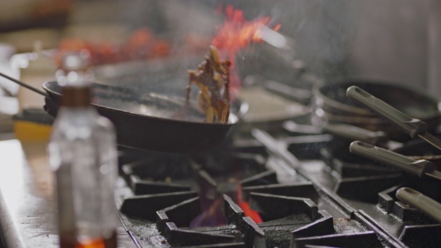 职业厨师在一家商业餐厅的厨房里，在燃烧的火炉上用平底锅煎香蕉。视频素材