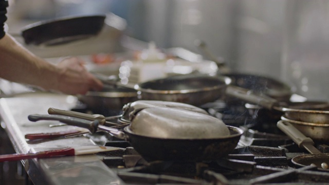 SLO MO:专业厨师在一个商业厨房里的燃烧的火炉上烹饪。视频素材
