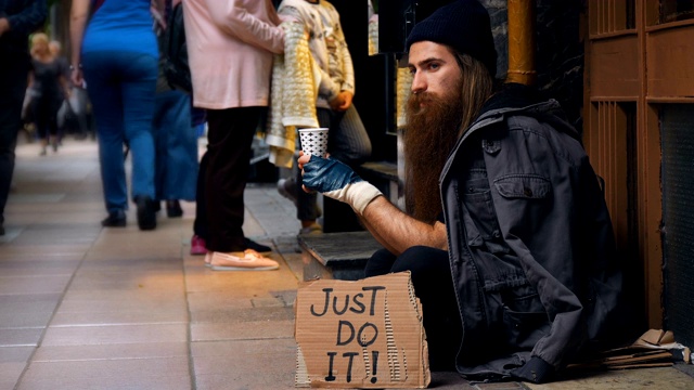 一个无家可归的人拿着“Just Do It”纸板，在拥挤的街道上乞讨视频下载