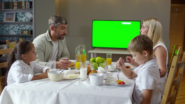 父母和孩子在吃早餐时聊天和看电视视频素材