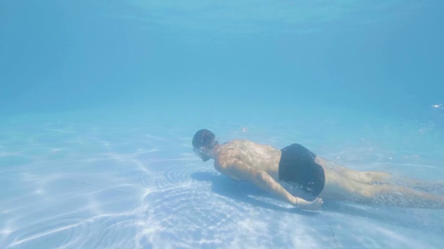 年轻男子在游泳池的蓝色水域跳水慢动作。水下视图男性游泳者在浮动池透明的水跳跃。视频下载