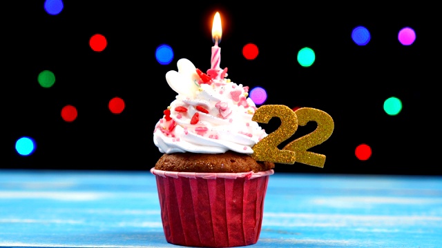 美味的生日蛋糕与燃烧的蜡烛和数字22在彩色模糊的灯光背景视频下载