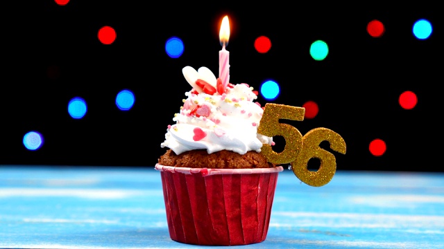美味的生日蛋糕与燃烧的蜡烛和数字56在彩色模糊的灯光背景视频素材