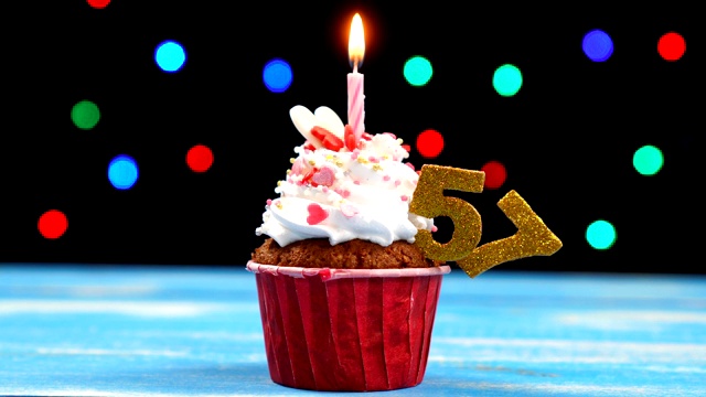 美味的生日蛋糕与燃烧的蜡烛和数字57在多色模糊的灯光背景视频素材