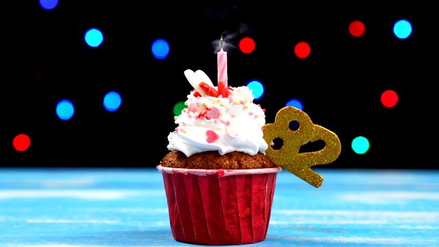 美味的生日蛋糕与燃烧的蜡烛和数字82在多色模糊的灯光背景视频素材