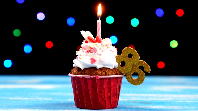 美味的生日蛋糕与燃烧的蜡烛和数字86在彩色模糊的灯光背景视频素材