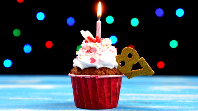 美味的生日蛋糕与燃烧的蜡烛和数字87在多色模糊的灯光背景视频素材